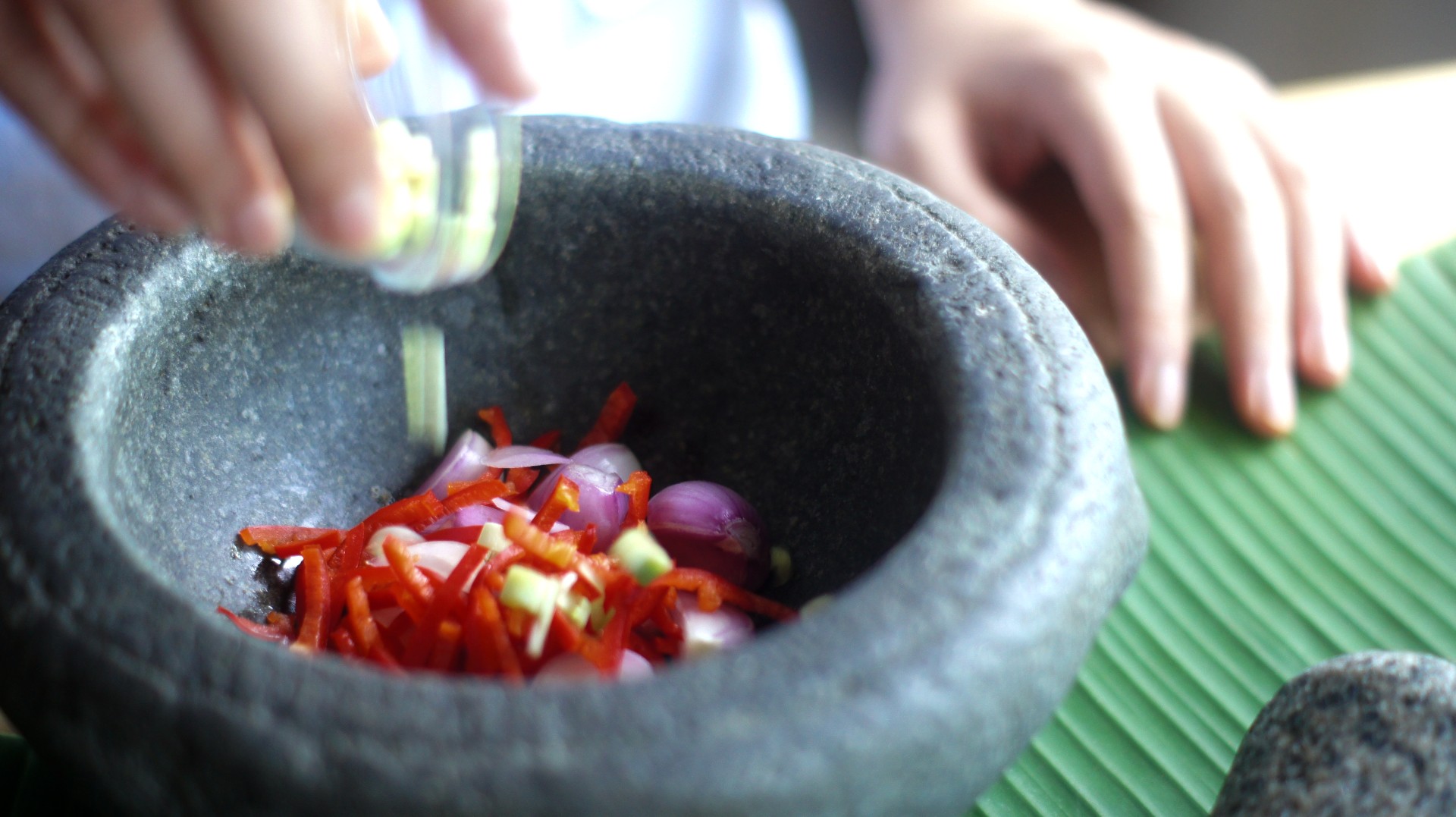 Adding shallots into the <em>batu lesung</em> to make the <em>rempah</em>. April 2020, photo by Wai Zi Ying.